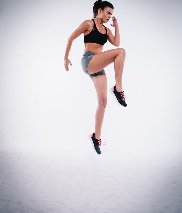 Woman in activewear performing a dynamic cardio movement in a modern studio.